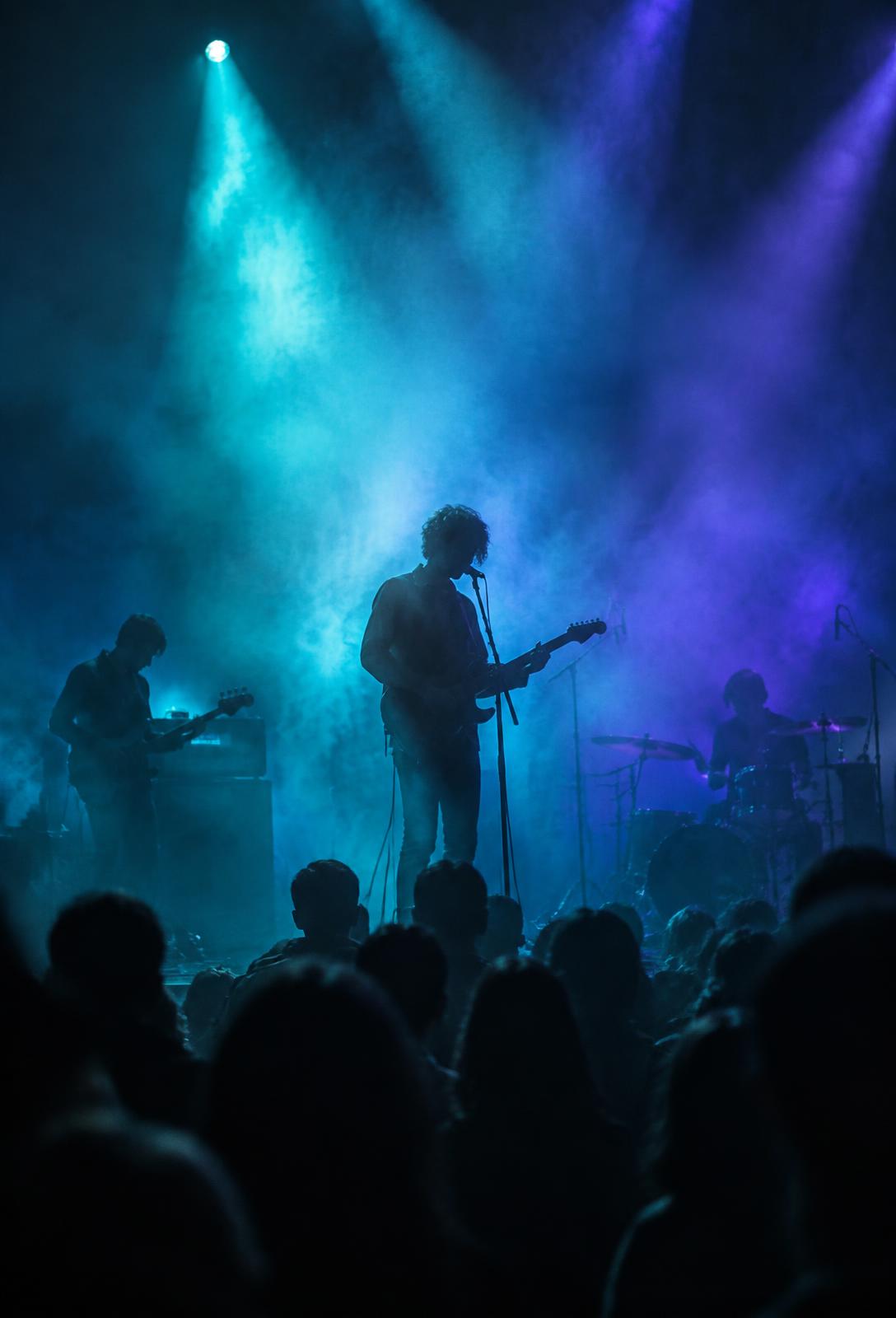 Band performing under teal and violet stage lights before a crowd